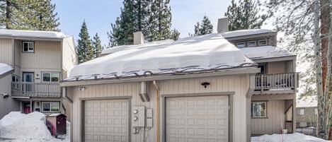 Un bâtiment à deux étages, dont le toit est recouvert de neige, avec deux portes de garage et une petite dépendance attenante.