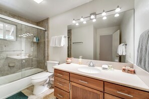Ein modernes Badezimmer mit einer gläsernen Duschkabine, einer weißen Toilette, einem Holzwaschtisch mit Waschbecken und einem großen Spiegel mit Beleuchtung.
