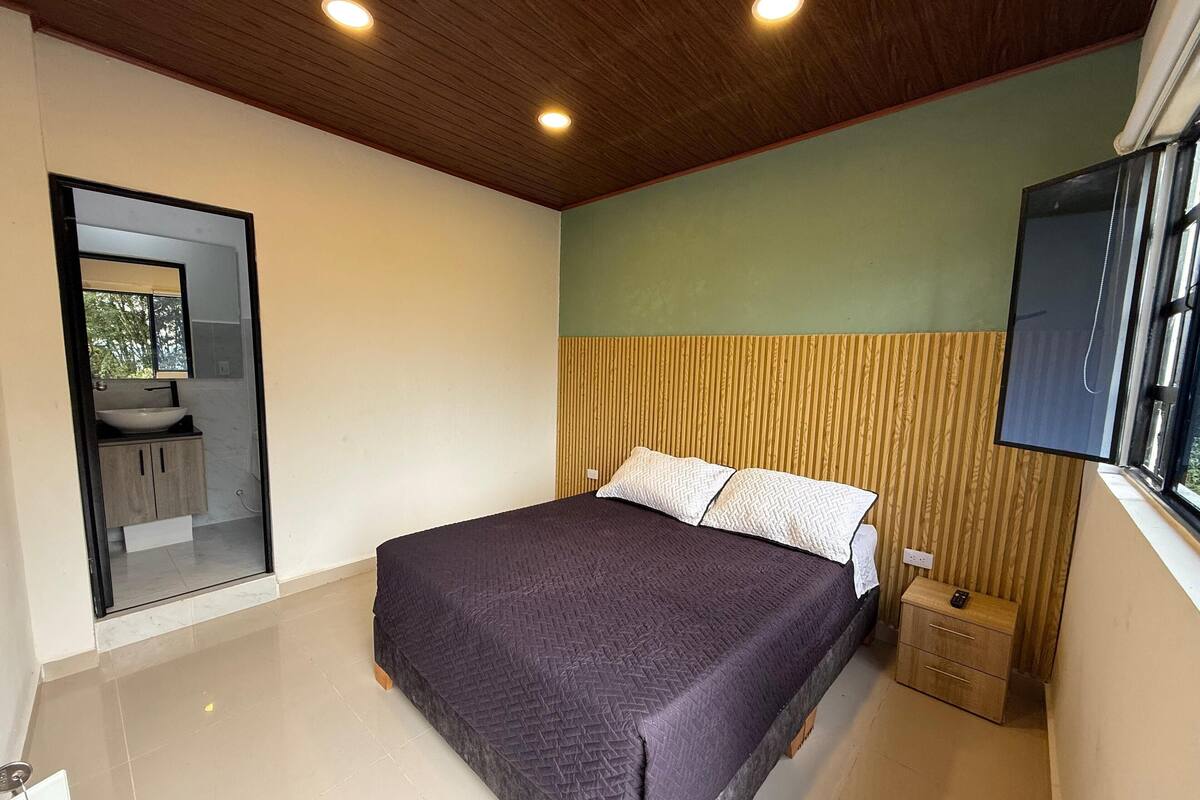 Een slaapkamer met een bed, nachtkastje, spiegel en raam.