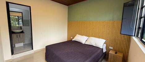 A bedroom with a bed, a bedside table, a mirror, and a window.