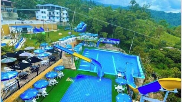 A pool area with slides and umbrellas, surrounded by lush greenery and buildings. - hotel piedra grande (San Antonio del Tequendama)