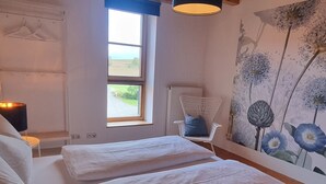Een slaapkamer met een groot bed, een stoel, een raam en een plafondlamp.
