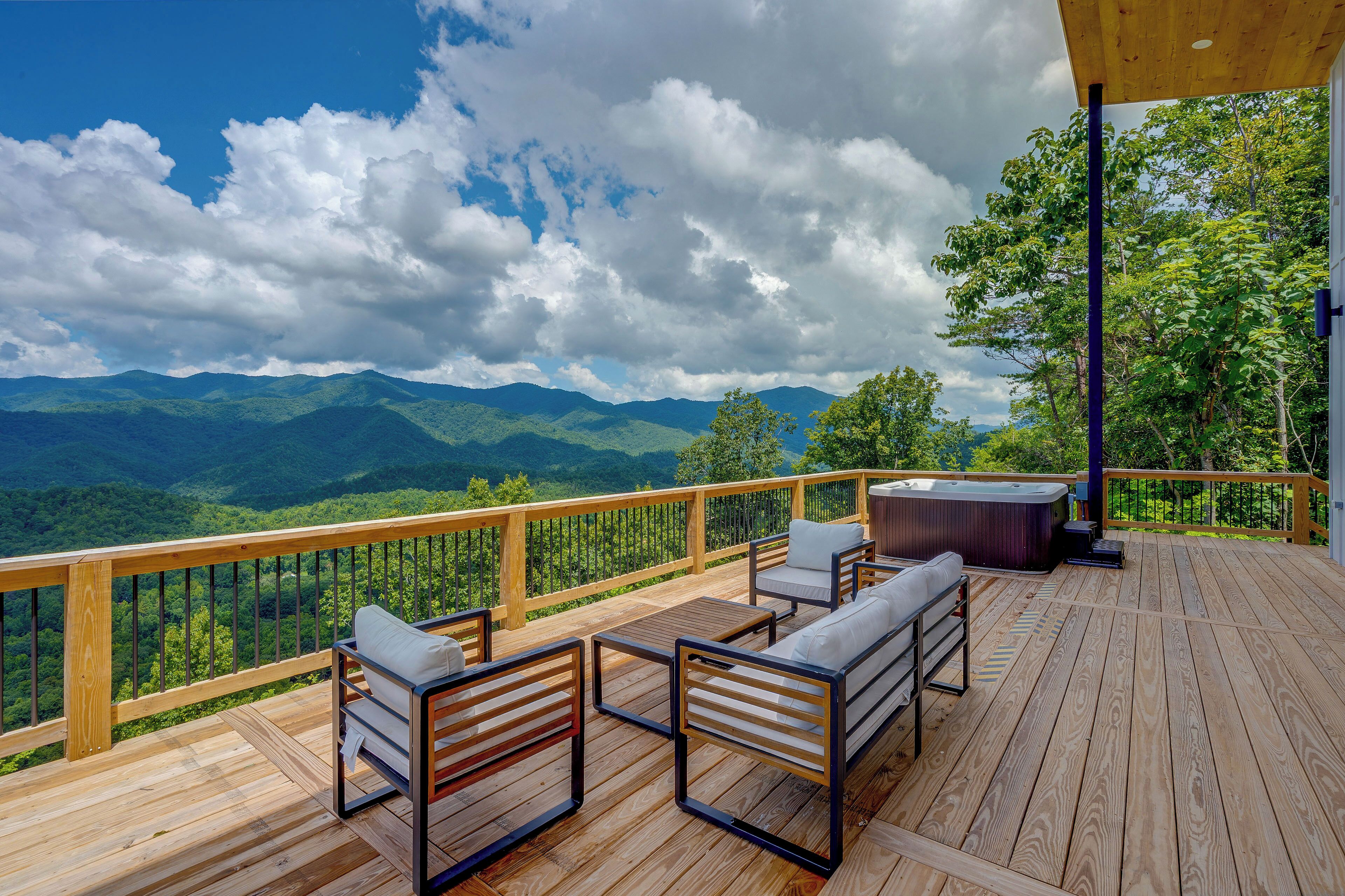 Un terrazzo in legno con mobili da esterno, una vasca idromassaggio e una vista panoramica sulle montagne.