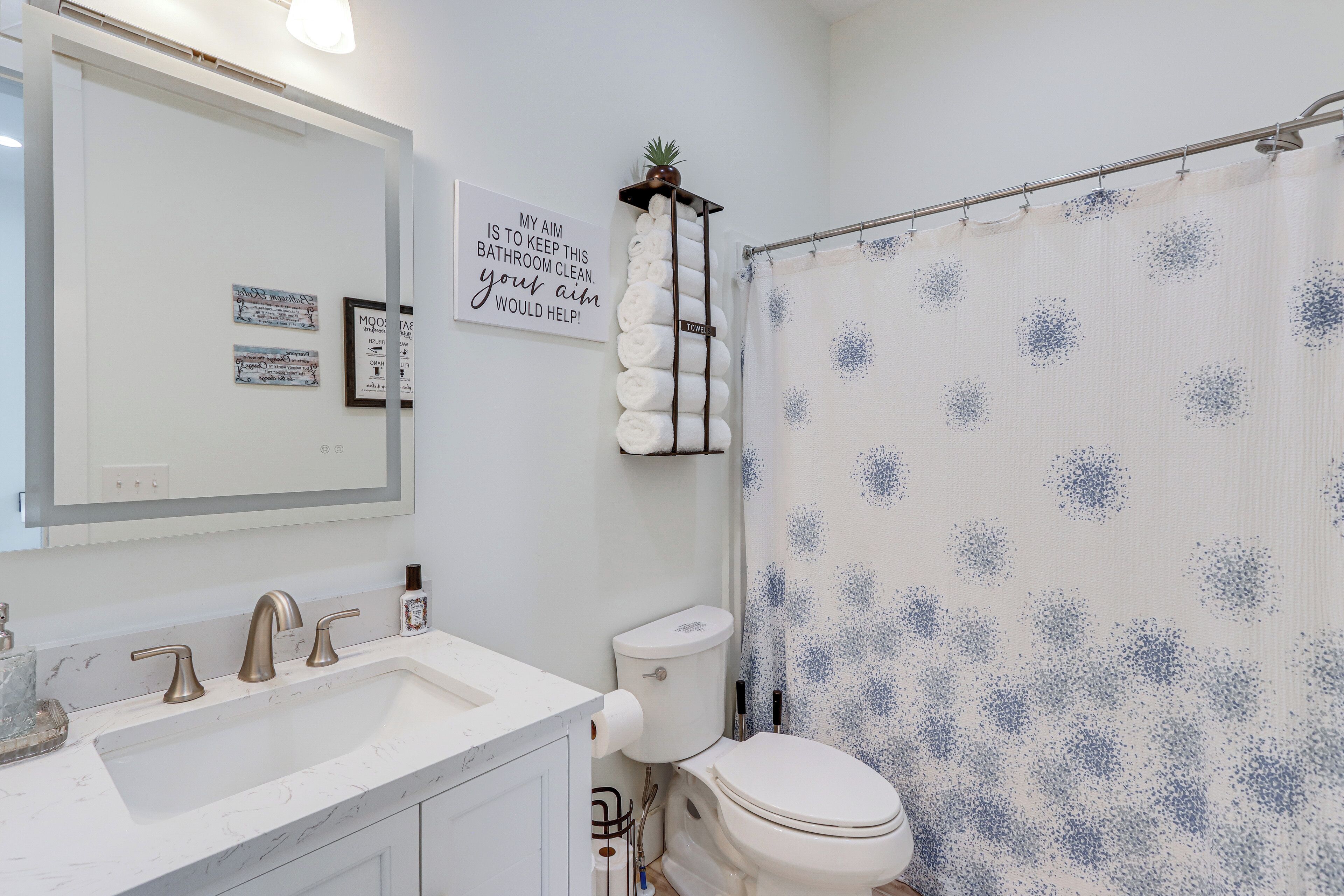 A bathroom with a white sink, two faucets, a toilet, and a shower curtain with a blue pattern.