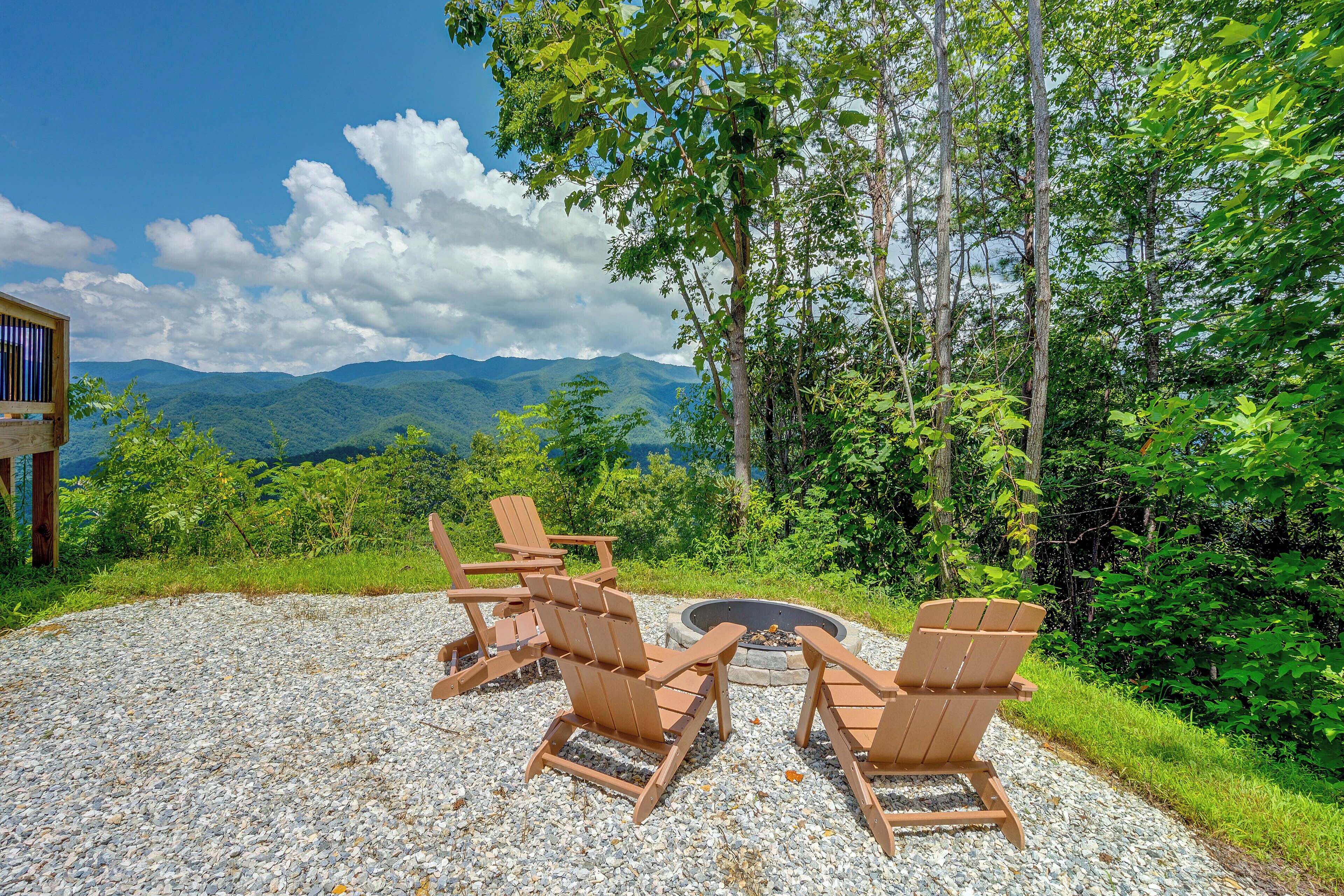 A gravel patio with Adirondack chairs and a fire pit, overlooking a mountainous landscape.
