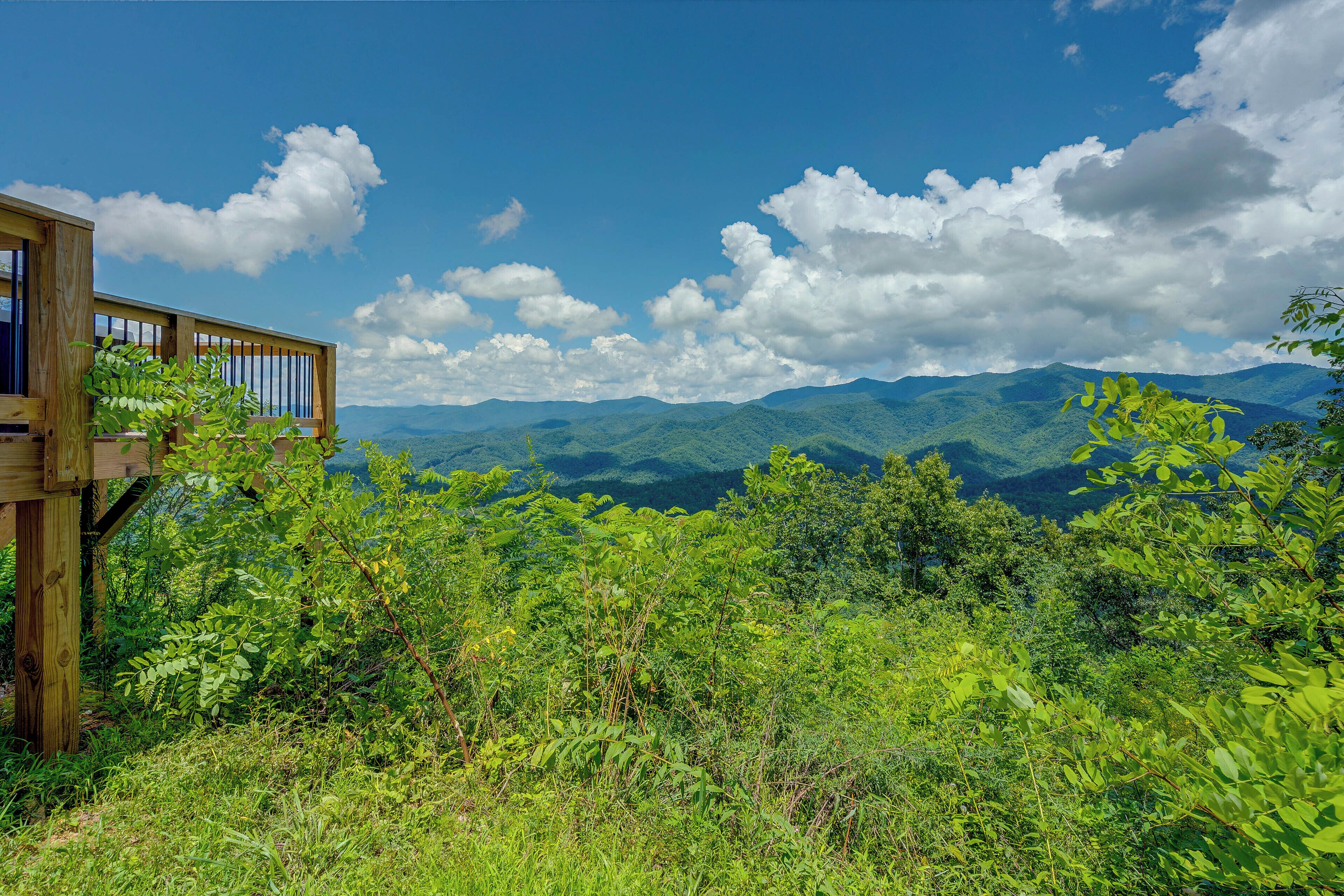 Una terraza de madera con vistas a un paisaje montañoso y abundante vegetación.