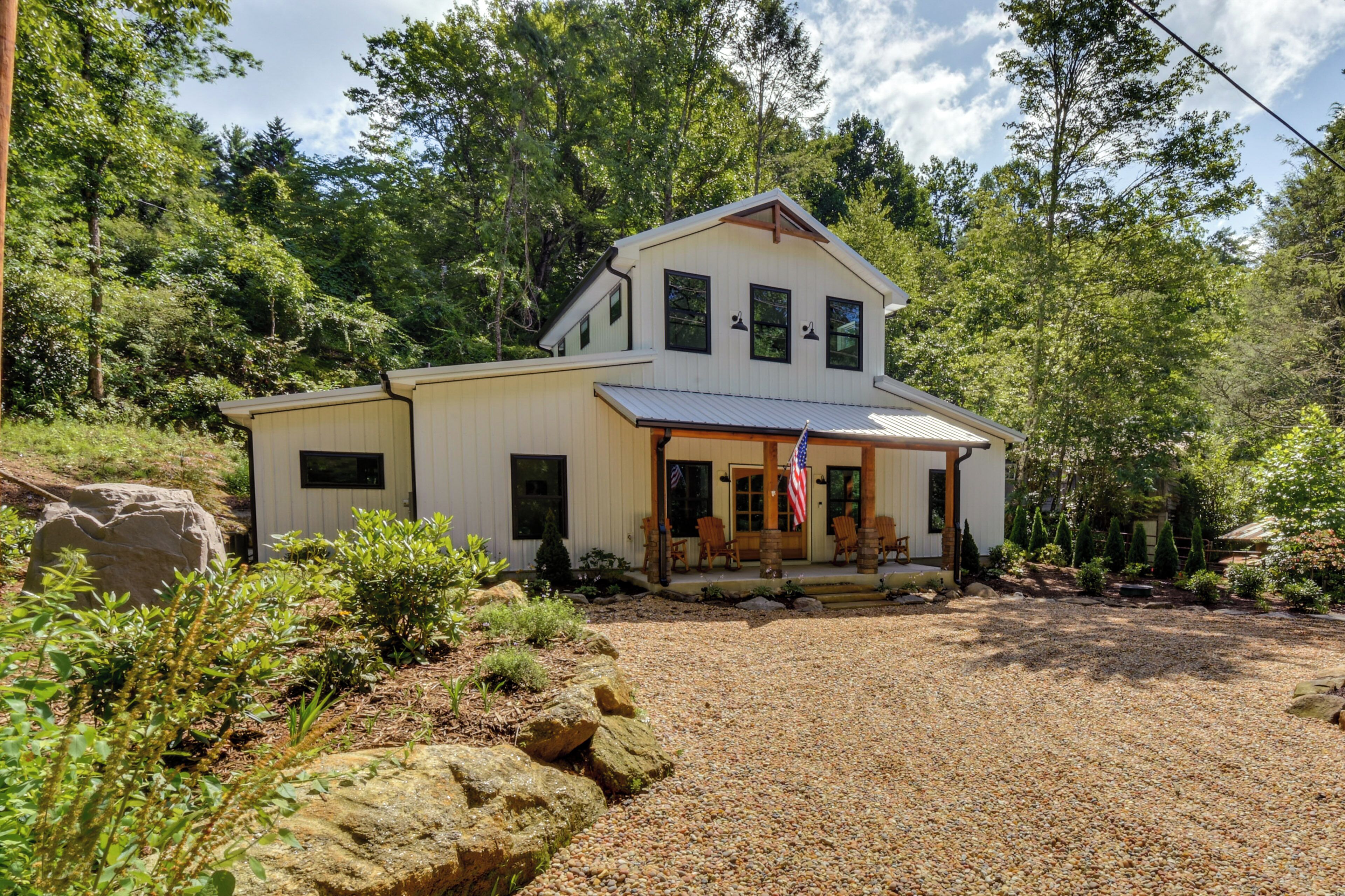 A two-story house with a porch, surrounded by a gravel driveway and a wooded area.