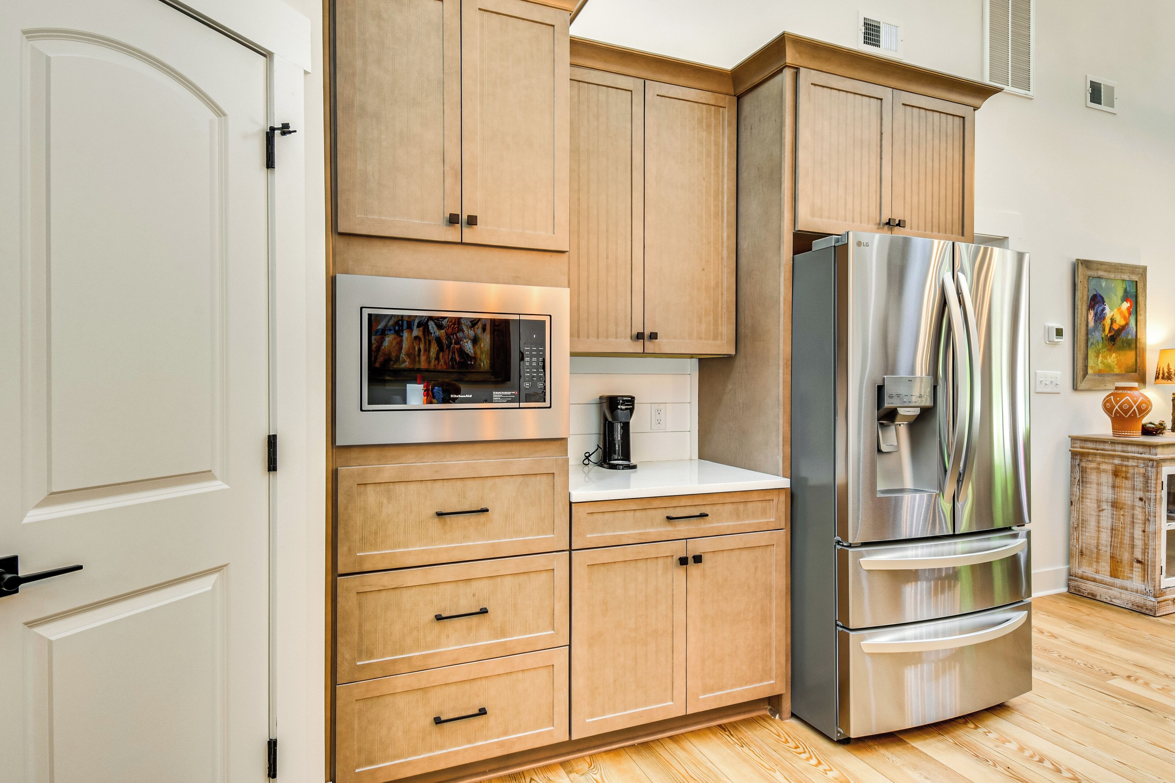 A modern kitchen with wooden cabinets, a stainless steel refrigerator, a built-in microwave, and a coffee maker.