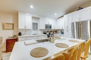 A modern kitchen with white cabinets, stainless steel appliances, and a wooden dining table with woven placemats. - 5 Mi to Stuart Beach! Home w/ Pet-friendly Yard (Stuart)