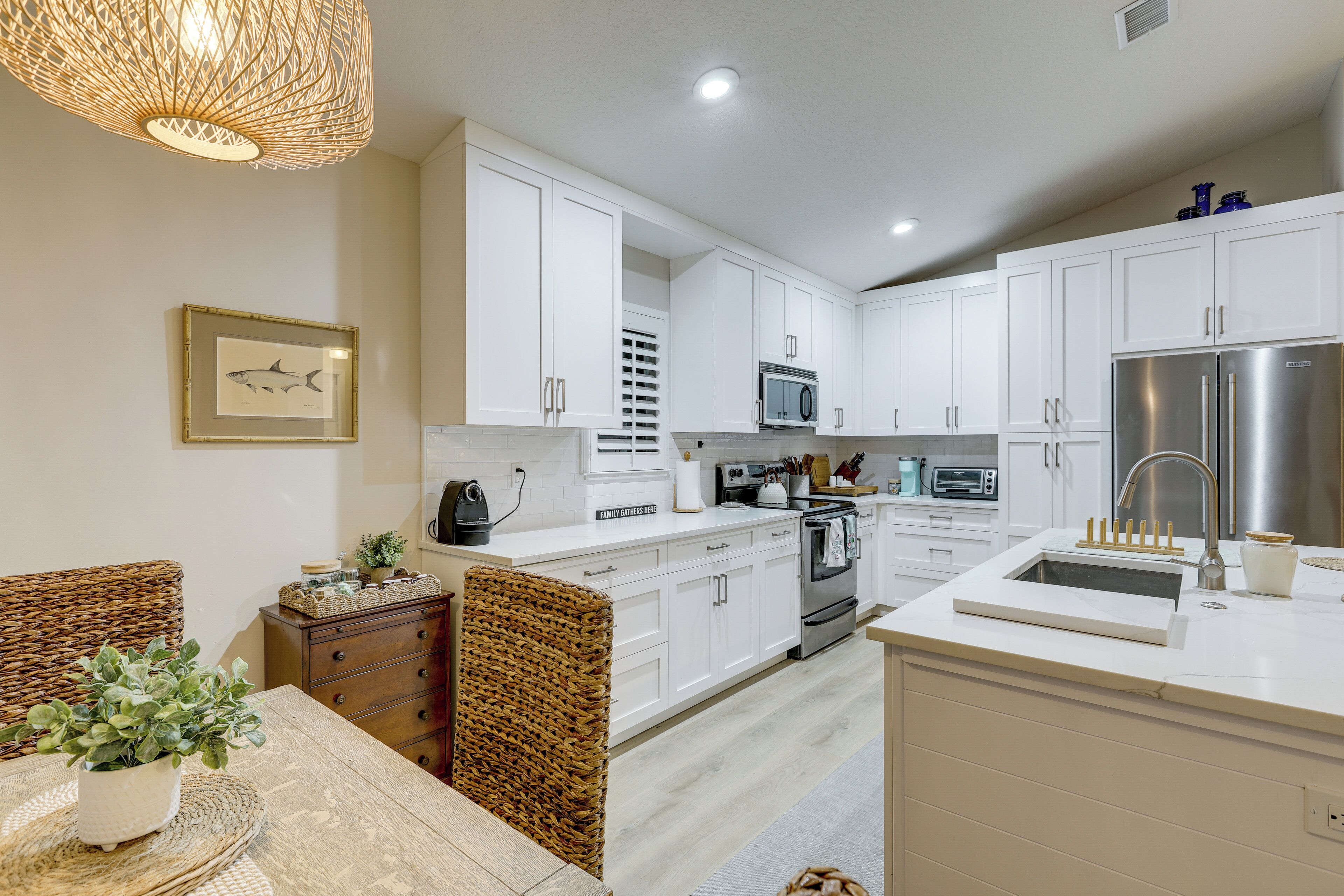 A modern kitchen with white cabinets, stainless steel appliances, and a wicker chair.