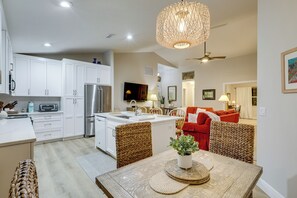 A modern kitchen with white cabinets, a stainless steel refrigerator, and a dining area with a wooden table and wicker chairs. - 5 Mi to Stuart Beach! Home w/ Pet-friendly Yard (Stuart)