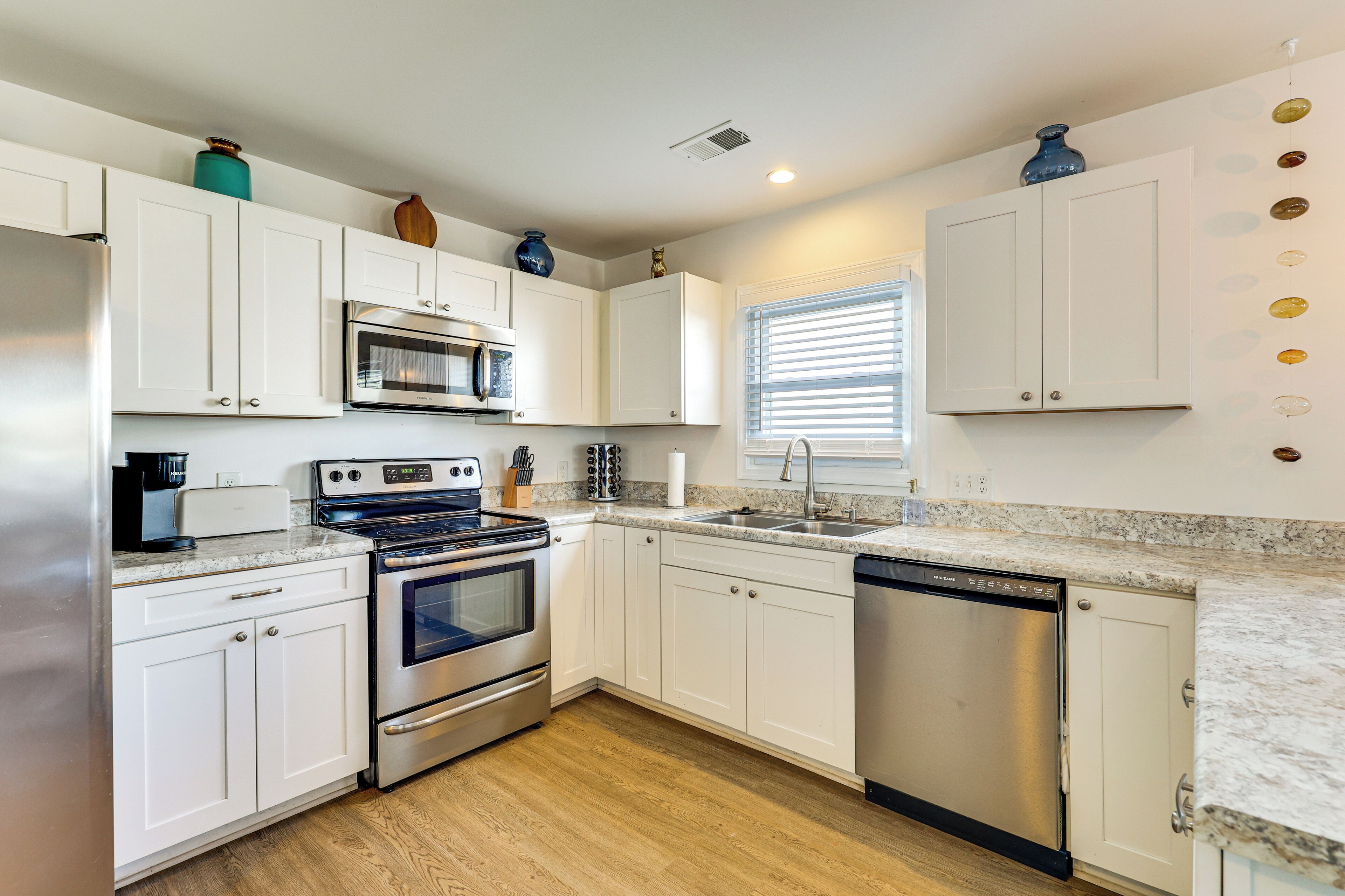 A modern kitchen with white cabinets, stainless steel appliances, a granite countertop, and a window with blinds.