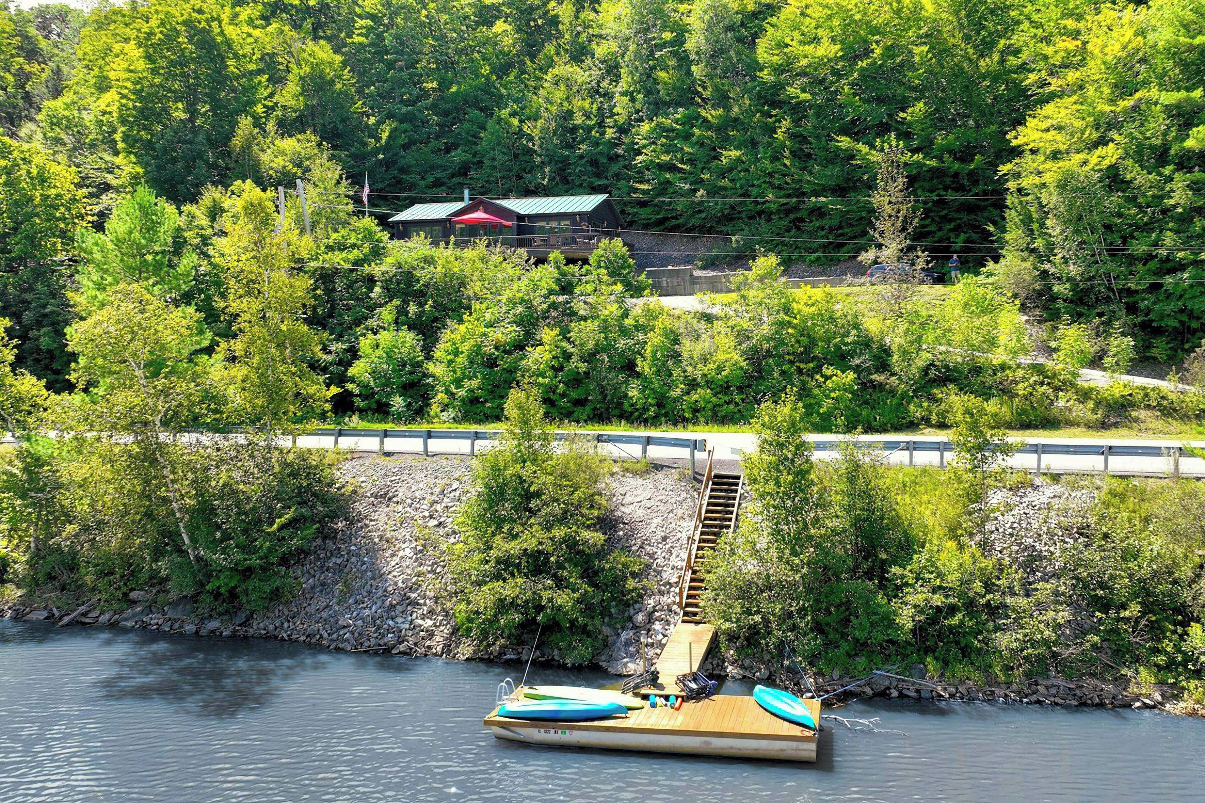 Une jetée en bois s’étendant dans une rivière, entourée d’une végétation luxuriante et, au fond, un bâtiment avec un toit rouge.