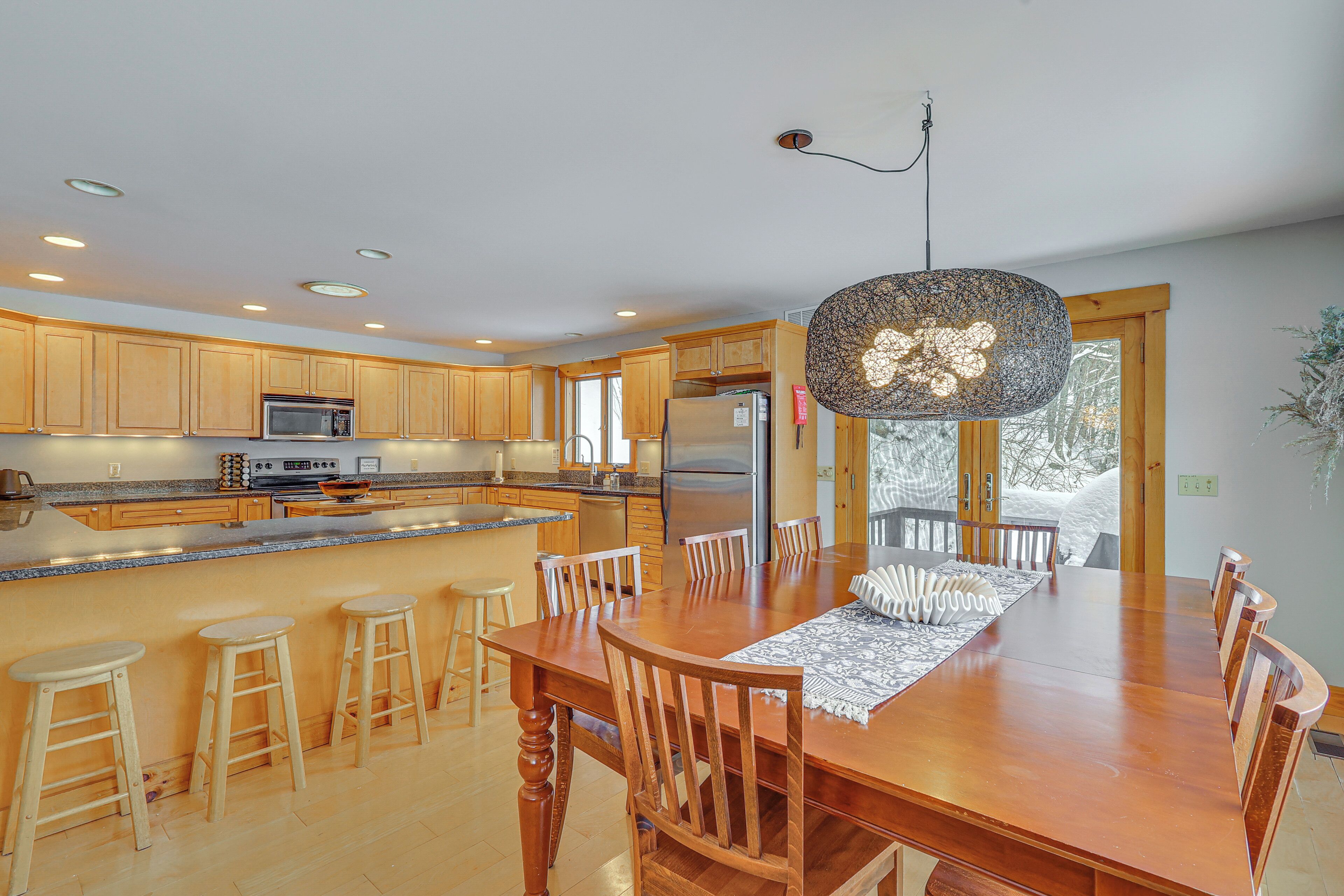 A modern kitchen with wooden cabinets, a large island with stools, and a dining table with chairs.