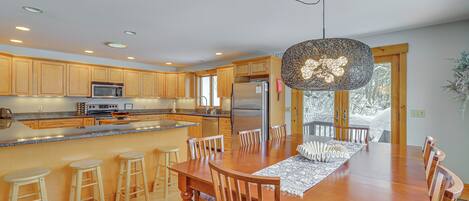 A modern kitchen with wooden cabinets, a large island with stools, and a dining table with chairs.