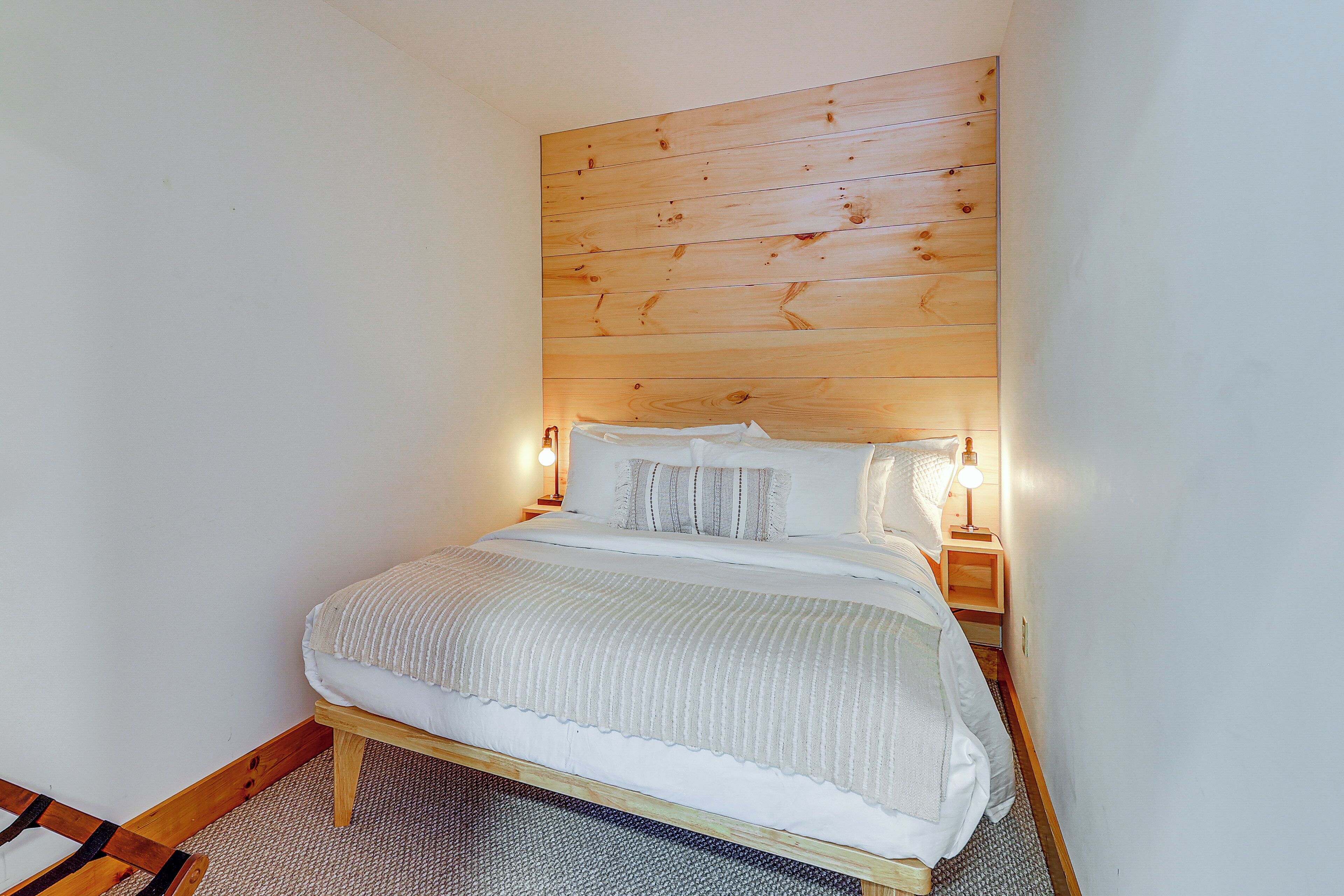Un dormitorio con cabecera de madera, una cama con ropa de cama blanca y dos lámparas de noche.