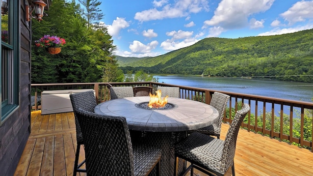 A deck with a round table and chairs, a fire pit, and a hanging flower basket. - All-season Lake House Between Okemo & Killington! (Plymouth)