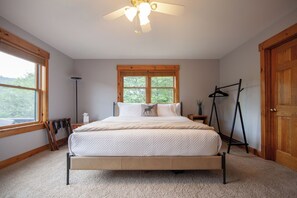 A bedroom with a bed, a window, a ceiling fan, and a door.