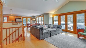 A spacious living area with a large gray sectional sofa, wooden flooring, and a view of a snowy landscape through large sliding glass doors. - All-season Lake House Between Okemo & Killington! (Plymouth)