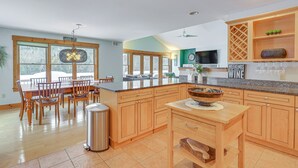 A spacious kitchen with wooden cabinets, a granite countertop, and a dining area with a large window. - All-season Lake House Between Okemo & Killington! (Plymouth)