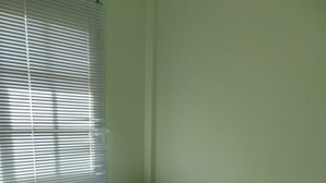 Una cama individual con un edredón estampado, una mesita de noche de madera con cajones y una ventana con persianas.