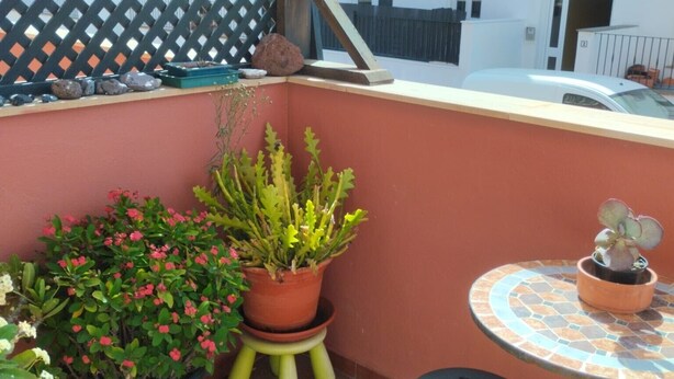 Un balcón con plantas en macetas, una mesita y una silla.