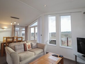 Un salon avec un canapé, une table basse et un téléviseur. Il y a de grandes fenêtres et un balcon avec vue.