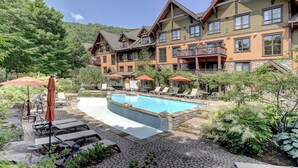 Hotel com piscina, área externa para sentar e paisagem montanhosa ao fundo.