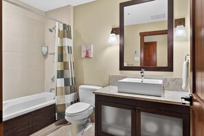 Un baño con bañera, inodoro, cortina de ducha, lavamanos y espejo.