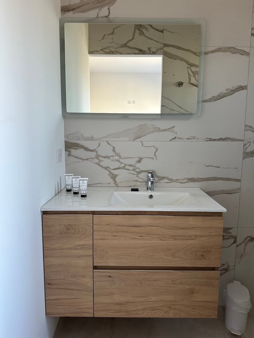 A bathroom with a marble wall, a white sink, and wooden cabinetry.