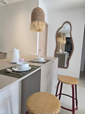 A modern kitchen with a central island, bar stools, a hanging light fixture, and a large mirror. - Les villas Vangarone (Lecci)