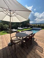 A wooden deck with a pool, lounge chairs, and a table with chairs.