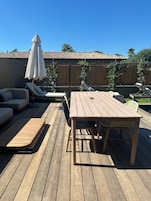 Una terraza de madera con una mesa, sillas y un sofá, además de una sombrilla.