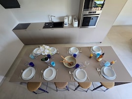 A modern kitchen with a dining table set for six, including plates, cutlery, and glasses.