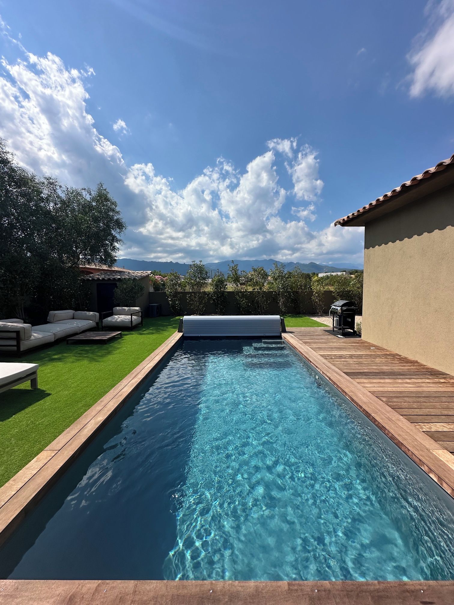 A rectangular swimming pool with a wooden deck on one side and a grassy area on the other.