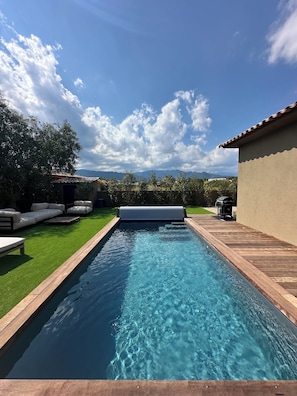 A rectangular swimming pool with a wooden deck on one side and a grassy area on the other.