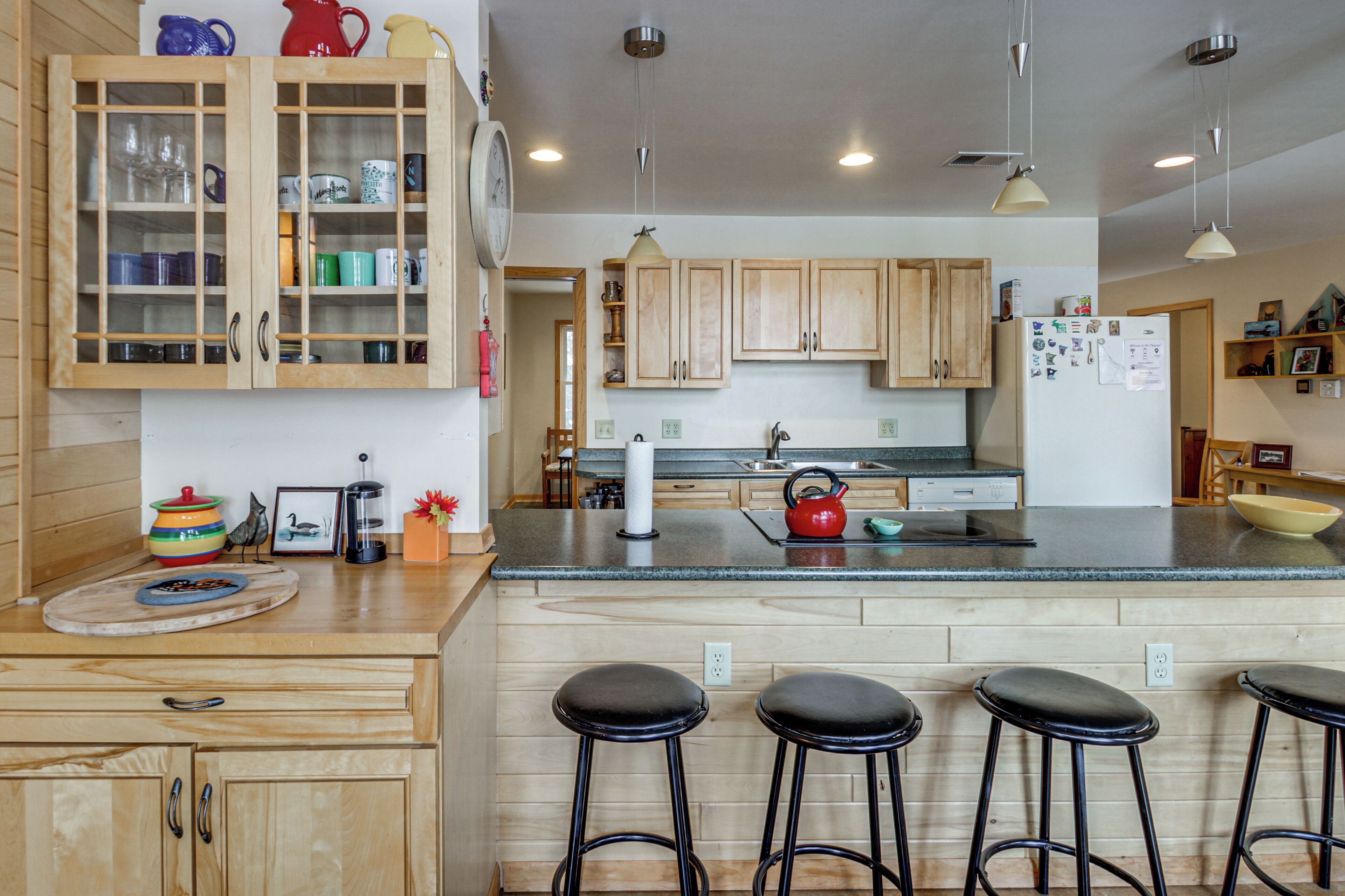 A modern kitchen with wooden cabinets, a central island with stools, and a refrigerator with magnets.