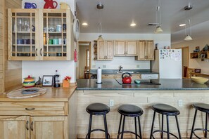 A modern kitchen with wooden cabinets, a central island with stools, and a refrigerator with magnets. - 4-season Recreation: Secluded Pike River Cabin (Tower)