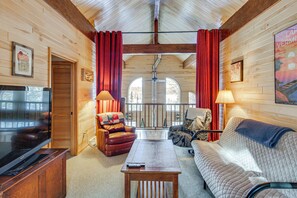 A cozy cabin interior with a wooden interior, a large window, a television, a sofa, a coffee table, and two lamps. - 4-season Recreation: Secluded Pike River Cabin (Tower)