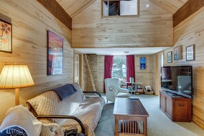 A cozy cabin interior with a wooden ceiling, a sofa, a chair, a table, a TV, and a window with curtains. - 4-season Recreation: Secluded Pike River Cabin (Tower)