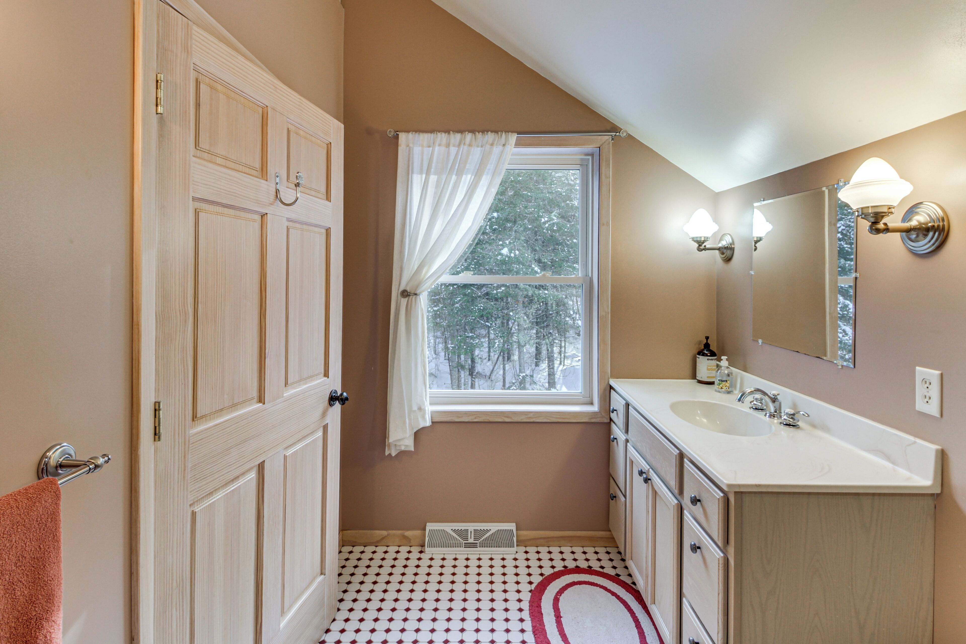 A bathroom with a window, a sink, a mirror, and a towel rack.