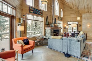 A cozy cabin interior with a stone fireplace, wooden walls, and large windows offering views of trees. - 4-season Recreation: Secluded Pike River Cabin (Tower)
