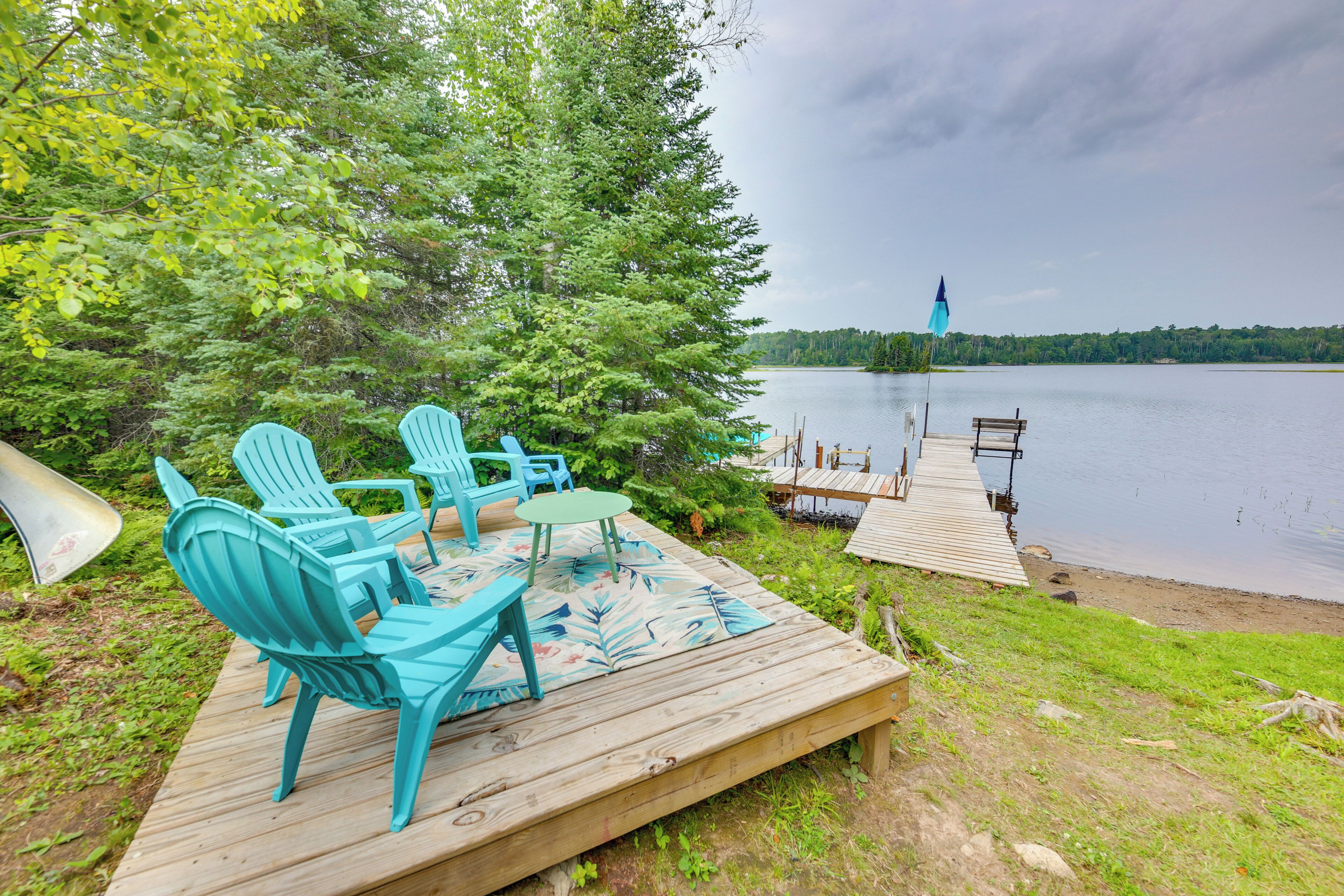 A wooden deck with outdoor furniture, a view of a lake, and a dock extending into the water.