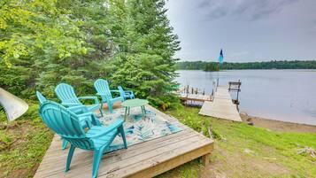 A wooden deck with outdoor furniture, a view of a lake, and a dock extending into the water.
