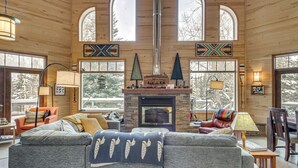 A cozy living room with a fireplace, wooden walls, and large windows.