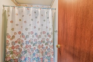 A bathroom with a shower curtain featuring a seashell pattern and a wooden door. - Relaxing Bayside Retreat in South Bethany w/ Porch, Bikes & Beach Access (South Bethany)
