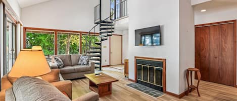 Amplia sala de estar con sofá, mesa de centro y chimenea. Una escalera en espiral conduce a un nivel superior.