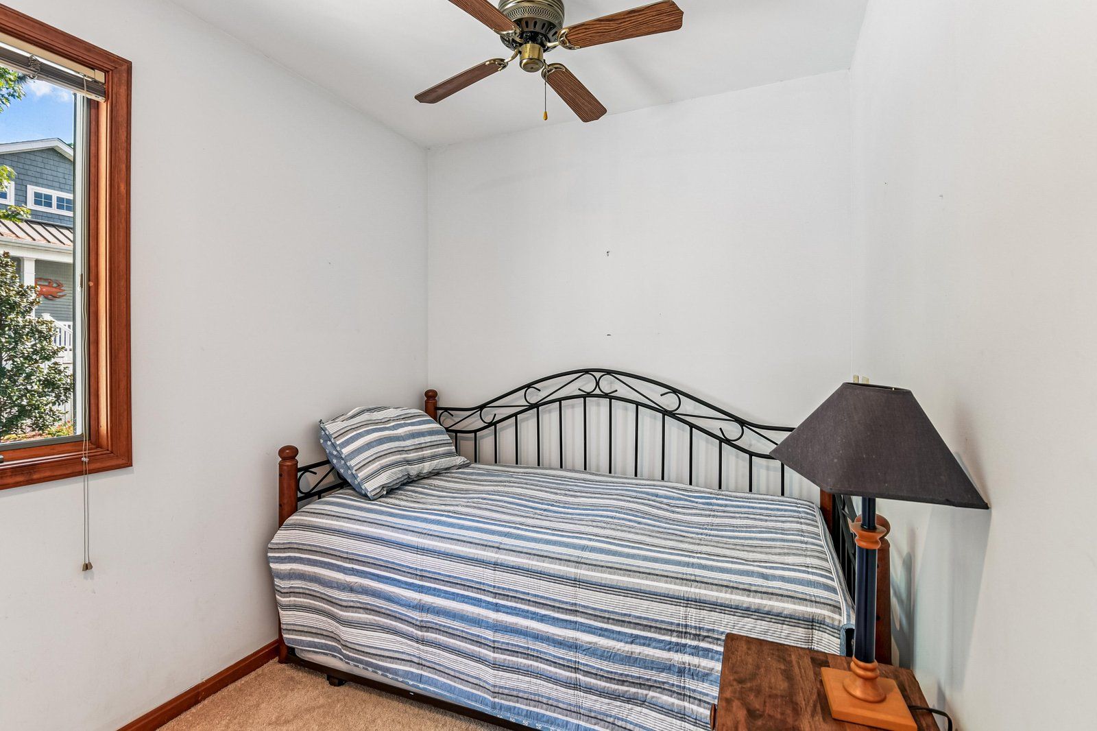A bedroom with a bed, a ceiling fan, a window, and a lamp.