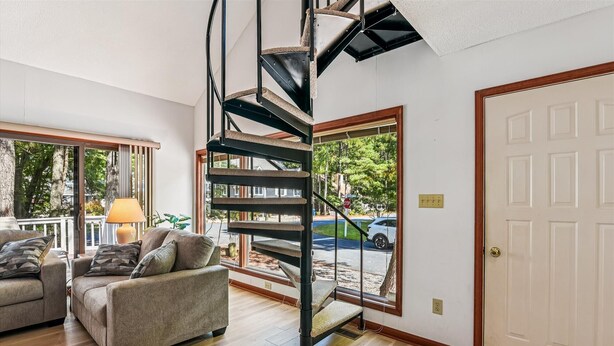A living room with a spiral staircase, a sofa, a lamp, and a view of the outside. - Relaxing Bayside Retreat in South Bethany w/ Porch, Bikes & Beach Access (South Bethany)