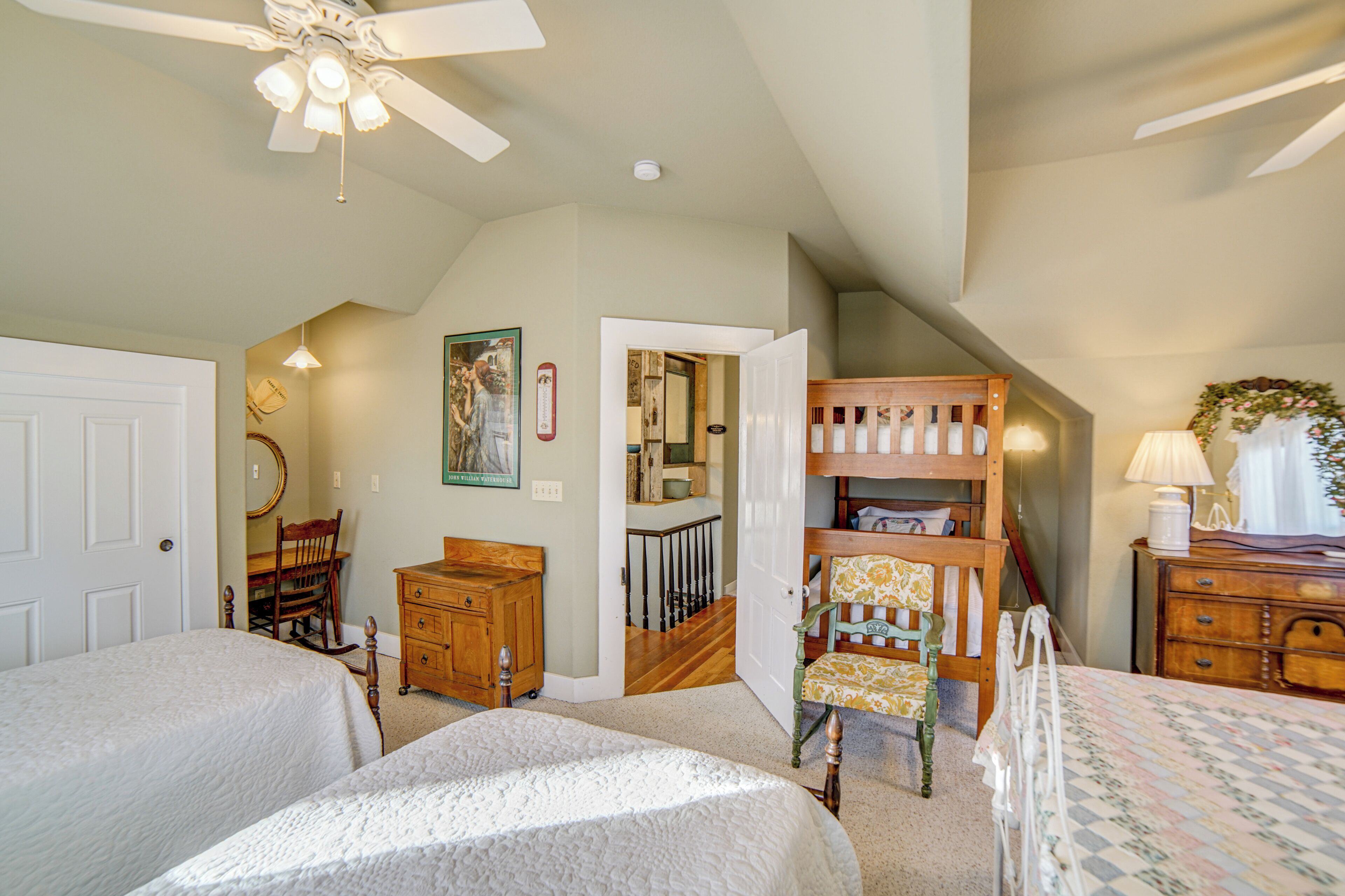 A bedroom with two beds, a wooden dresser, a chair, a ceiling fan, and a door leading to another room.